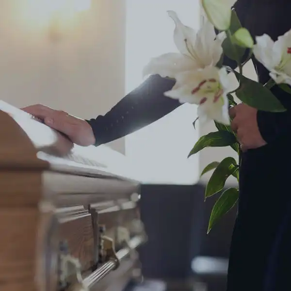 Man holding flowers, with his other hand on a closed casket.
